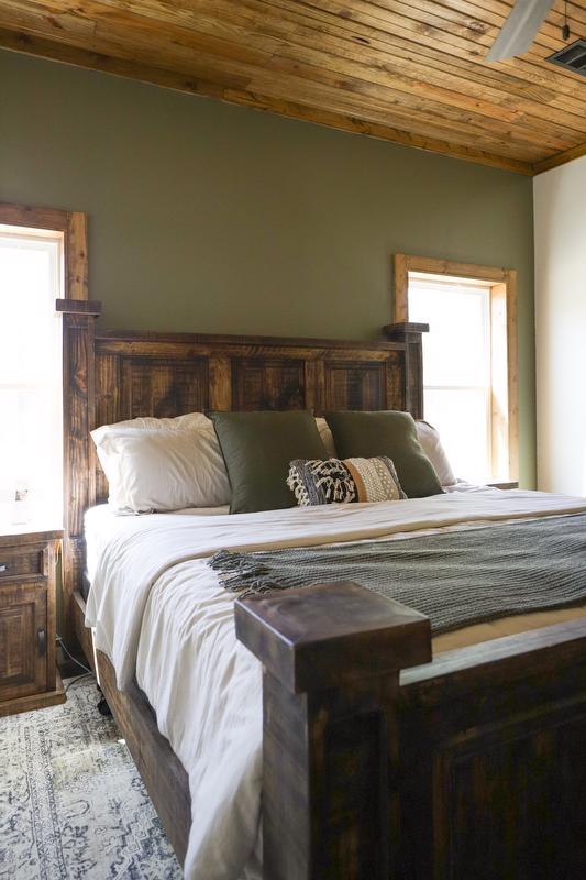 Bedroom area with large bed, olive green wall, and warm stained wood ceiling.