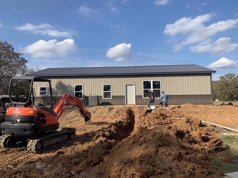 Exterior of home with heavy equipment moving dirt. Two men walk near the house.