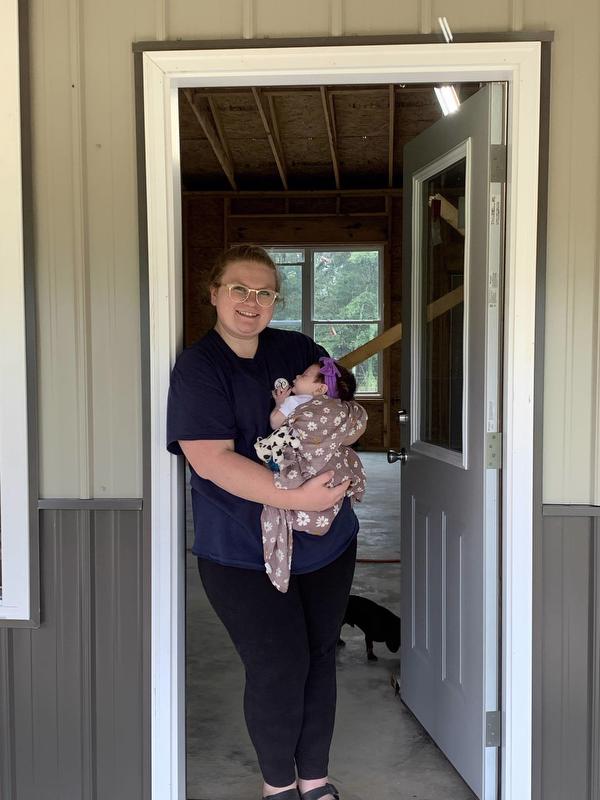 Emilie holds infant Hattie in the door frame of home under construction