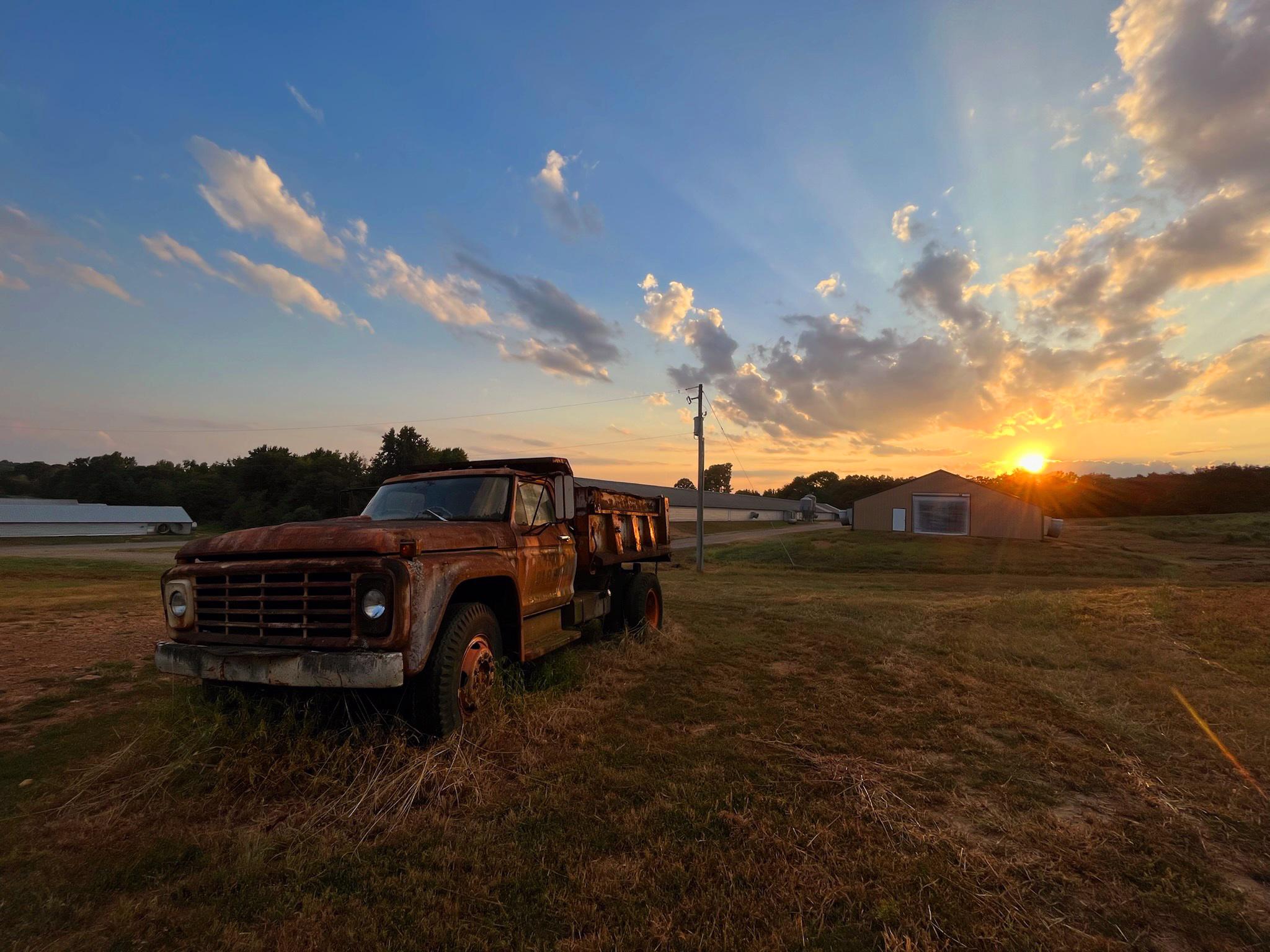 Rusty truck in a field at sunset